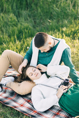 A guy and a girl love each other, smile, hug, kiss, laugh, enjoy life in the forest on a cliff, in the grass. Girl holding a film camera in her hands, photographs a guy, sunset in the background.

