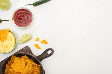 top view of corn nachos with lime, chili peppers, ketchup and cheese sauce  on wooden cutting board on white background