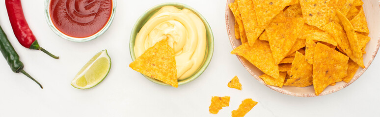 top view of corn nachos with lime, chili peppers, ketchup and cheese sauce on white background, panoramic shot