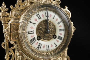 Fototapeta na wymiar dial of vintage bronze clock on black background, antique clock photo close up, old bronze clock in gilding, twelve o'clock on the dial 