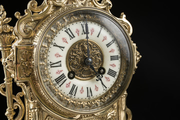 dial of vintage bronze clock on black background, antique clock photo close up, old bronze clock in gilding, the fifth hour on the dial, five o'clock on antique clock