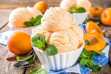 Homemade sweet apricot ice cream. Apricot gelato balls in small bowls, on wooden background with fresh apricots and mint leaves