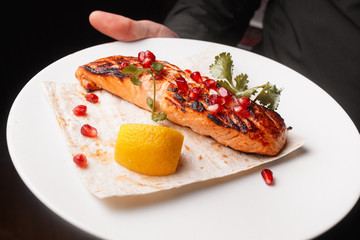 Grilled salmon steak on a white plate served with pita and lemon