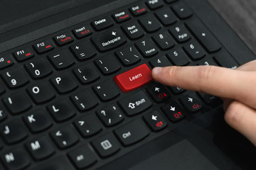 Index finger presses the red button on the black laptop keyboard. Computer keyboard with red key...