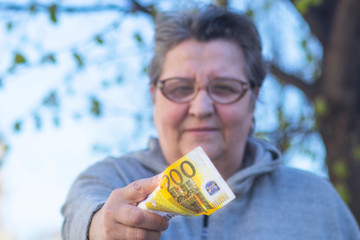 An elderly adult woman gives a currency of close-up 200 euros. Mature woman and holds out a bill. Senior female. Concept Retired pensioners and money.