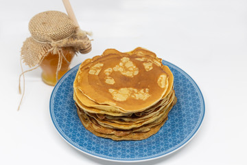 A pile of pancakes in a blue plate and a honey pot, white background