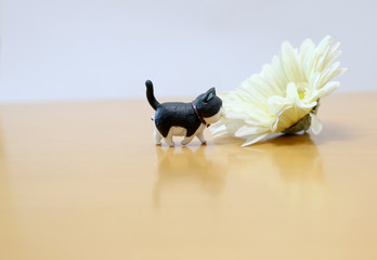 A small resins cat toy with a beautiful flower on table.