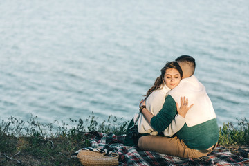 A guy and a girl love each other, smile, hug, kiss, laugh, enjoy life in the forest on a cliff, in the grass. Girl holding a film camera in her hands, photographs a guy, sunset in the background.
