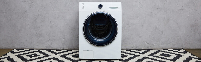 panoramic shot of modern washing machine near grey wall and ornamental carpet in bathroom