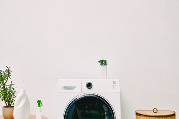 green plant and bottles on coffee table near washing machine and laundry basket in bathroom