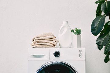 Detergent bottle and towels on washing machine and green plant in bathroom - obrazy, fototapety, plakaty