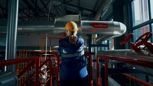 Woman worker in a factory in a helmet and uniform rotates a huge red valve