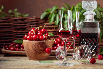 Cherry liquor and red cherries in a wooden bowl on a wooden table.
