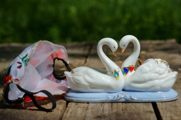 Colored gauze mask on a wooden surface. Two souvenir swans next to a medical mask.