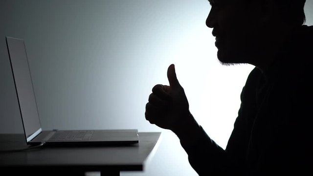 Silhouette asian man Working on Laptop. Beared man Works from home on Notebook. Freelancer man Blogger Working remotely at Home With Laptop. A Man looking and thump up face.