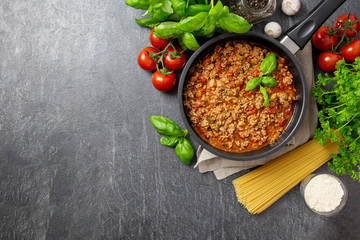 Traditional italian Bolognese sauce in sauce pot. Parmesan cheese, tomatoes, basil, spices and herbs. Dark background. Top view. Copy space.