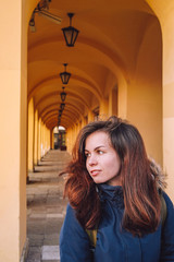 Fototapeta na wymiar A young woman in a jacket stands against the background of multiple arches in a yellow building