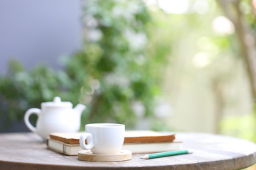 White tea kettle and white cup with notebook and pencil on wooden table outdoor view