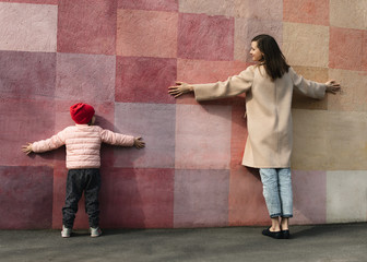 Obraz na płótnie Canvas Mom and daughter play against a multi-colored wall, look at each other with a smile