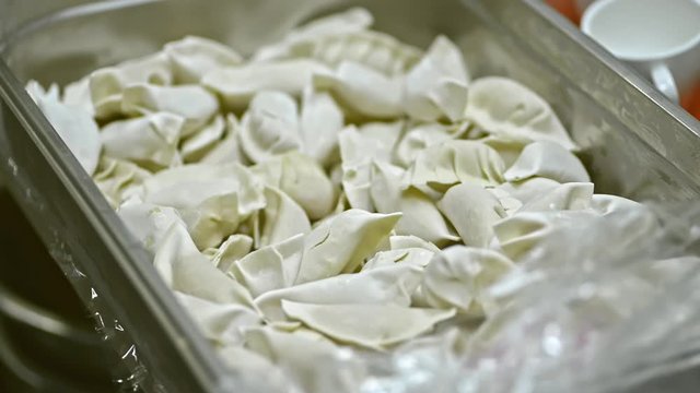 steel catering container with frozen raw dumplings from fridge lrrl. in cafe restaurant. concept small business, preparation, traditional meal. dough gedza vareniks