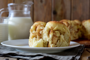 A piece of yeast cake with cinnamon on a beautiful plate in the foreground and a glass jug of milk in the background on a wooden table