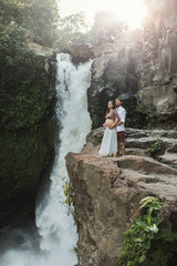 Childbirth in Bali. Young pregnant couple travel on Tegenungan waterfall. Family harmony values. Happy together, pregnancy travel lifestyle. Beautiful morning nature. Maternity concept.