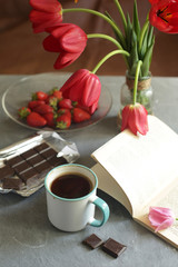Fototapeta na wymiar On the table is a cup of coffee, chocolate bar, a book and flowers. 