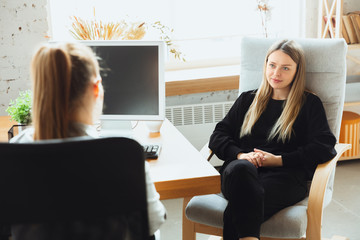 Young woman sitting in office during the job interview with female employee, boss or HR-manager, talking, thinking, looks confident. Concept of work, getting job, business, finance, communication.