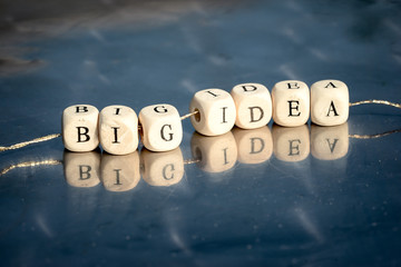 Wooden cubes with big idea inscription strung on a thread on reflective table.