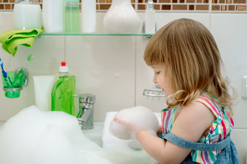 bath foam baby.Cleaning the bathroom. Foam in the washbasin, green soap and green gloves in the girl. Clean house. cleaning up. child washes plumbing.
