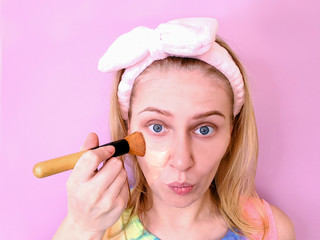 Makeup. A young woman in a multi-colored T-shirt applies foundation on her face with a makeup brush...