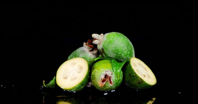 Whole and halves of fresh feijoas slowly rotate.