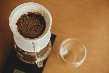 Drip coffee. Brewing aromatic fresh coffee in paper filter closeup in pour over on scale. Alternative coffee brewing v60 closeup. Barista making filter coffee on brown background
