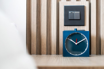 Square blue analog alarm clock on table in bedroom. Minimal clock style.
