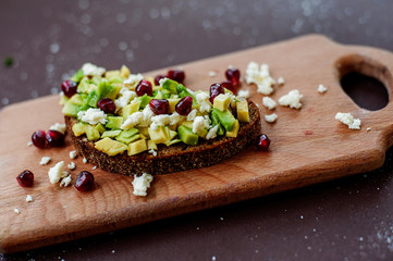 Sandwich with avocado, cottage cheese and pomegranate seeds on cutting board on table close up. Healthy food concept. Selective focus.
