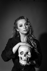 vertical closeup portrait of a fatal blonde with a human skull in her hands