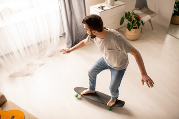 Above view of young man performing balance training on skateboard at home during isolation period