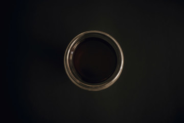 Fresh coffee in glass cup on black background flat lay with copy space. Minimalism. Drip or filter coffee. Dark moody image. Coffee brewing. Glass circle