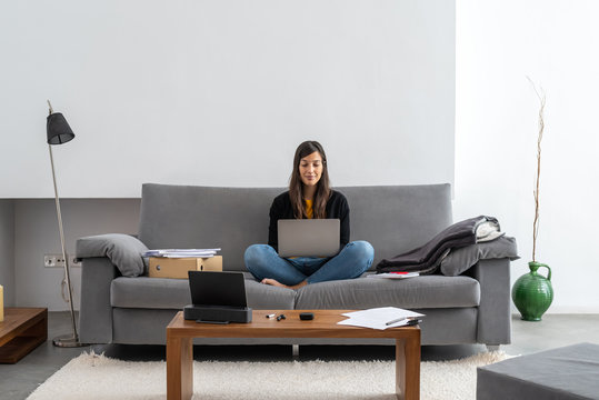 Young woman with laptop telecommuting on the sofa at her home