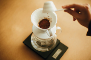 Hands pouring grounded coffee in filter pour over on glass kettle on scale. Preparing for...