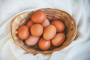 A small wicker basket with a few brown chicken eggs lies on a soft white cloth. Preparation for the celebration of Easter.