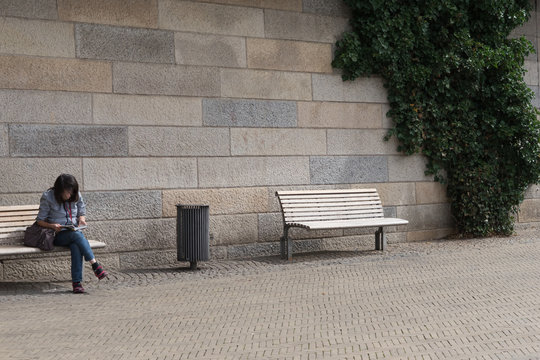 Frau mit Mundschutz einsam auf einer Bank an der Ufer-Promenade liest ein Buch