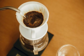 Pouring hot water from steel kettle in filter with ground coffee in pour over on scale. Alternative coffee brewing v60 closeup. Barista making filter coffee on brown background