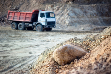 Pile of ore rocks over out of focus background with heavy multi-ton heavy mining truck exporting minerals from open-pit mine. Concept of shipping and protecting the environment and nature.