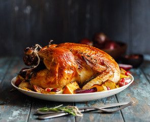 Roast whole chicken with roast vegetables on plate on a table