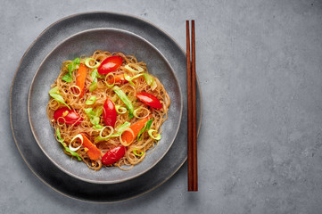 Veg Pad Woon Sen or Thai Glass Noodle Stir-Fry or Pad Thai in bowl on gray concrete backdrop. Vegetarian Pad Woon Sen is a Thai dish of glass bean noodles, tomatoes, carrots, egg, sauces. Thai Food.