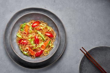 Veg Pad Woon Sen or Thai Glass Noodle Stir-Fry or Pad Thai in bowl on gray concrete backdrop. Vegetarian Pad Woon Sen is a Thai dish of glass bean noodles, tomatoes, carrots, egg, sauces. Thai Food.