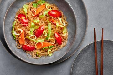 Veg Pad Woon Sen or Thai Glass Noodle Stir-Fry or Pad Thai in bowl on gray concrete backdrop. Vegetarian Pad Woon Sen is a Thai dish of glass bean noodles, tomatoes, carrots, egg, sauces. Thai Food.