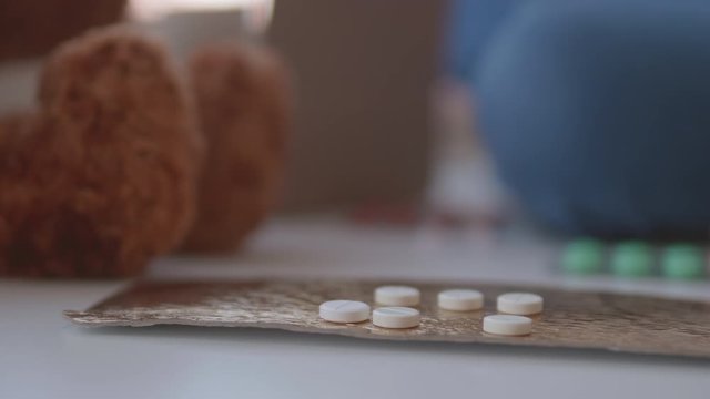 Kid plays with scattering medicine drugs. Toddler touches pills without parent control. Dangerous situation.