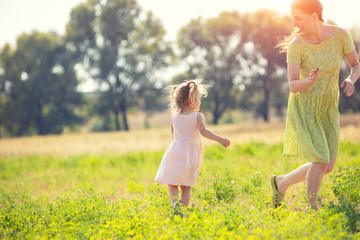 Fototapeta na wymiar Happy mother walking with little daughter outdoors in summer. The mother and kid run in the field. Happy childhood (family) and Mother's Day concept